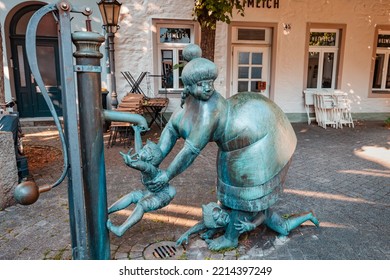 24 July 2022, Osnabruck, Germany: Funny Statue Of A Family With A Mother And Kids Near A Water Pump