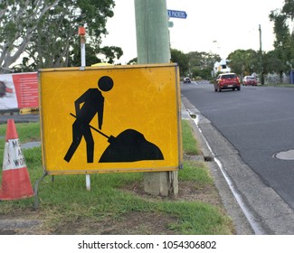  24 March 2018, Coffs Harbour, New South Wales, Australia. Yellow Sign Board Of Working Man And Men At Work Cone At Work Site Placed Beside Road With Moving Cars In Australia                          