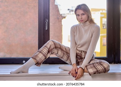 24 Year Old Woman In Checkered Pants Sits On Windowsill.