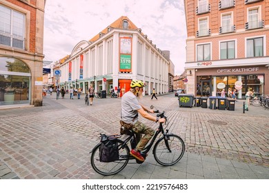 25 July 2022, Munster, Germany: Motion Blur Of An Elderly Man Rides A Bicycle In A Helmet On A Bike Sidewalk Path Near Museum Of Munster