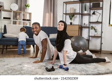 25-30 Age Beautiful Sporty Couple Practicing Yoga Doing Four-limbed Staff Pose At Home. Muscular Athletic African Man And Beautiful Muslim Fitness Woman In Workout Clothes Doing Push Up Exercises.