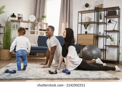 25-30 Age Beautiful Sporty Couple Practicing Yoga Doing Four-limbed Staff Pose At Home. Muscular Athletic African Man And Beautiful Muslim Fitness Woman In Workout Clothes Doing Push Up Exercises.