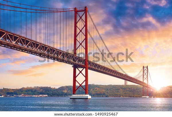 25th April Bridge in Lisbon, Portugal. Famous\
landmark on river Tagus. Summer sunny landscape with evening dusk\
sunset sky with clouds and\
sunlight.
