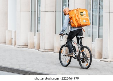 26 July 2022, Munster, Germany: A Male Courier On A Bicycle With A Large Backpack With Food Carries An Order Made Through A Mobile Application To A Client