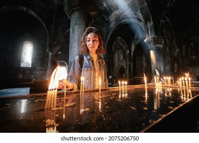 26 May 2021, Geghard, Armenia: Woman Puts A Candle And Prays In A Church Or Catholic Church. The Concept Of Sorrow And Hope In Faith