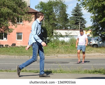 26th Of July 2018 - Scene From Russian City With View Past Young Guy Waling Along The Pavement To Man In Shorts Crossing The Road, Kingisepp, Russia       