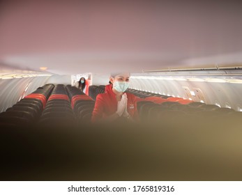 28 Jun 20, Donmueng Airport, Bangkok, Thailand. Female Cabin Crew In Red Uniform Greeting Passenger In Aircraft Cabin During Boarding. Cabin Crew In Medical Mask Greeting Passengers During Covid 19.