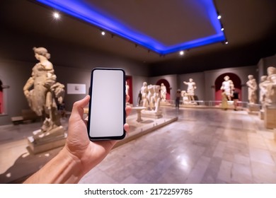 28 May 2022, Antalya, Turkey: Smartphone With A Blank Screen In The Interior Of An Archaeological Museum With Antique Greek Statues. Concept Of An Audio Guide And E-learning Mobile Application