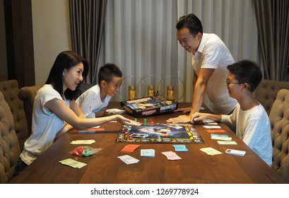 29th December 2018, Bangkok Thailand. Asian Family Playing Monopoly Board Game Together At Night. Father, Mother, Older Son And Younger Son Enjoying The Game.