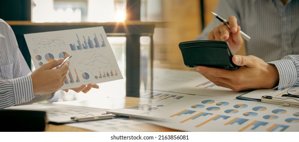 2Businessmen Analyze Financial Sales Data And Economic Growth Charts, Make Money And Calculate Expenses With A Desk Home Office Calculator Graph Document.