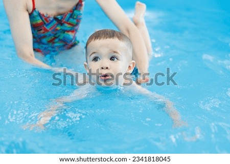 A 2-year-old boy learns to swim in a pool with a coach. Swimming lessons for children. Swimming school for children. Educational swimming courses for children