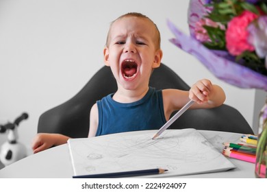 A 2  year  old child draws and colored pencils in an album   screams  Bad mood  Expression emotions by child through drawing 