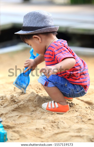 2-year-old Thai boy wearing\
jeans Red striped T-shirt, blue stripes playing in sand and\
children\'s play car