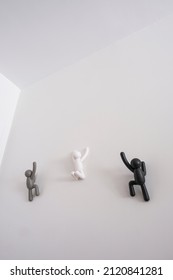 3 Black, Grey And White 3D Puppets Climbing Over A White Wall, Concept Of Self Improvement And Help Each Other And Message Of Equality And Non Discrimination To The Race, Vertical