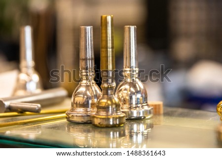 3 Brass mouthpieces arranged on a glass shelf at a music repair shop. A trumpet, trombone, and euphonium mouthpiece.