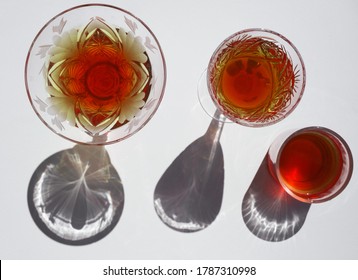 3 Crystal Glasses With Bright Red Filling Inside On A Light Background. View From Above. Bright Sun, Interesting Shadows. The Atmosphere Of Celebration And Fun. Delicious Summer Cool Desserts