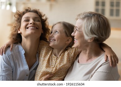 3 generations women. Overjoyed happy little girl embrace shoulders of laughing mother smiling older grandmother. Loving family of three diverse age females spend time together hug on sofa having fun