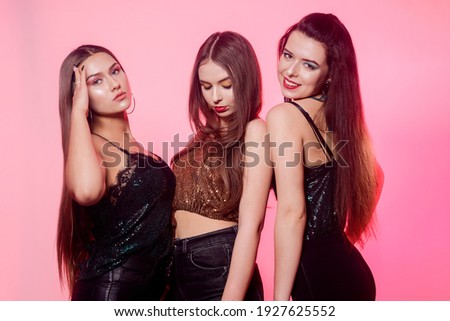 3 girls posing, laughing on a pink background. Girls in brilliant dresses with different colorful makeup. Three brunette girls dance and enjoy life. March 8, women's power, Women's Day