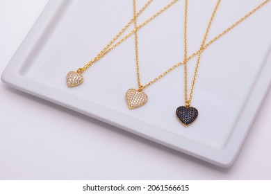 3 Gold Necklaces On A White Plate On A Soft White Background.