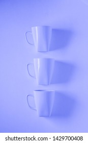 3 Monochromatic Blue Coffee Mugs Lined Up In A Row On Blue Background With Blank Empty Room Space For Text, Copy, Or Copyspace. Modern Top View Concept Of Three Cups With Solid Background Backdrop