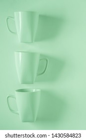 3 Monochromatic Green Coffee Mugs Lined Up In A Row On Green Background With Blank Empty Room Space For Text, Copy, Or Copyspace. Modern Top View Concept Of Three Cups With Solid Background Backdrop