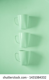 3 Monochromatic Green Coffee Mugs Lined Up In A Row On Green Background With Blank Empty Room Space For Text, Copy, Or Copyspace. Modern Top View Concept Of Three Cups With Solid Background Backdrop