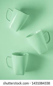 3 Monochromatic Green Coffee Mugs Scattered On Green Background With Blank Empty Room Space For Text, Copy, Or Copyspace. Modern Top View Concept Of Three Several Cups With Solid Background Backdrop