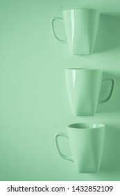 3 Monochromatic Green Coffee Mugs Lined Up In A Row On Green Background With Blank Empty Room Space For Text, Copy, Or Copyspace. Modern Top View Concept Of Three Cups With Solid Background Backdrop