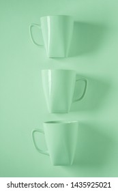 3 Monochromatic Green Coffee Mugs Lined Up In A Row On Green Background With Blank Empty Room Space For Text, Copy, Or Copyspace. Modern Top View Concept Of Three Cups With Solid Background Backdrop