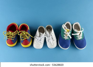 3 Pair Of Baby Shoes Lined Up On Blue Background With Space For Copy