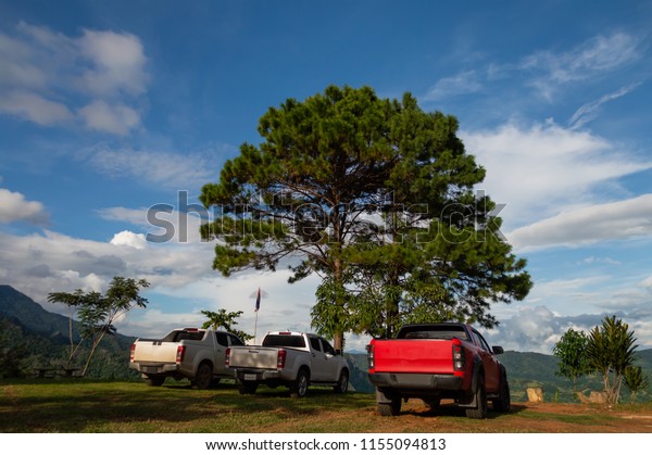 The 3 pickup truck, mobility vehicles parked on\
the soil ground It\'s a mountain point of travel attraction in\
Thailand, with background of mountain range, white clouds and blue\
sky, Beautiful nature.