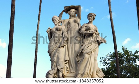 3 statues of women representing the arts as muses with palm trees in the background 