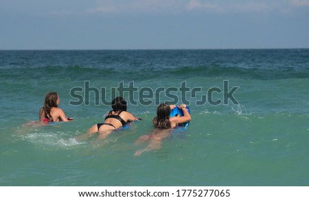 3 teenage girls ride waves on boogie boards in the ocean.