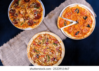 3 types of pizza in 1 frame with a black background and pieces of burlap, there are peppercorn pizza, margarita pizza, and tuto pizza - Powered by Shutterstock