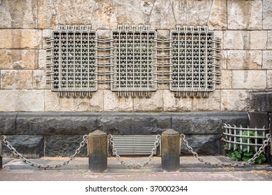 3 windows behind the metal bars in the wall of an ancient building with cast iron chains between the stone pillars in the pavement in front - Powered by Shutterstock