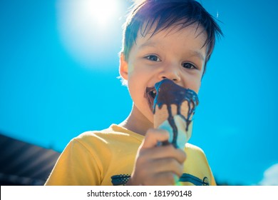 3 year old asian caucasian boy enjoying a melting chocolate ice-cream on a sweltering hot summer day. Clear blue summer sky in background - Powered by Shutterstock