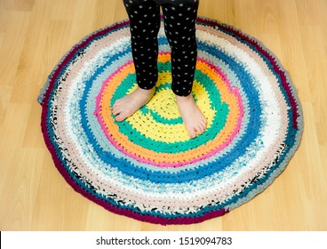 3 Year Old Young Child Standing On Round Colorful Crochet Rug From Repurposed T-shirts On Brown Wooden Home Floor. Top Above View.