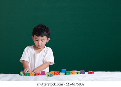 3 Years Old Asian Boy Play Toy Or Square Block Puzzle On Green Chalkboard Or School Board Background, Kid Lying Learn By Playing Block Shape Or Pieces, Education Concept Idea.