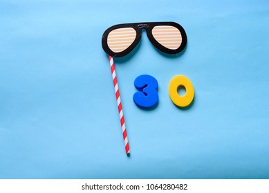 30 celebrating yellow number with sunglasses cute paper mask on straw stick . Thirty Modern alphabet digits on blue background. 30 th birthday party anniversary card.Flat lay, top view.