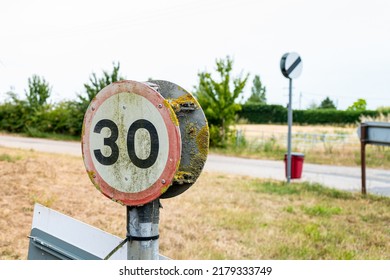 30 Mph sign showing detail of its heavy weathering. Seen with other road signs at an intersection at the outskirts of a rural village.
