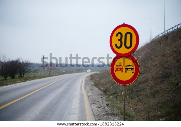 A 30\
speed limit and NO OVERTAKING sign along the\
road
