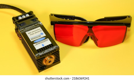 30 watt diode laser for cutting and engraving with blue ray. Diode laser and red safety glasses on yellow background isolated.