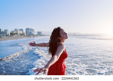 30 Year Old Latin Woman Standing In The Sea Water With Her Arms Open And Eyes Closed Enjoying The Sunset And Breeze