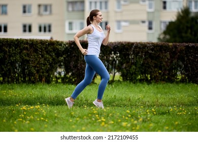 30 Year Old Woman Is Jogging In City Park On Summer Day.