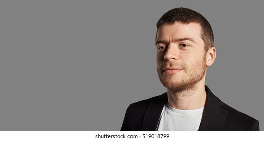 30 Years Man Portrait On Neutral Grey Background. Face With A Grin. European Man In A Black Jacket And White Shirt. Happy Student Photo. Copy Space For Advertising Text.