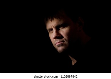 30-35 Year Old Man Portrait In A Dark Key In Half-profile Concentrated And Serious With Bristle Looking In The Camera. Unshaven Young  Squinting Handsome Man Standing At Gaze. Toughts At  Night. 