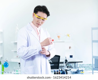 30s Asian Scientist Or Researcher Wear Transparent Yellow Safety Goggles Glasses While Adjust Wrist White Gown Uniform Before Experiment And Research Biotechnology And Chemistry Testing Job In Lab