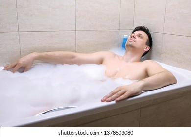 30s man sitting in the bathroom, relaxing and falling asleep in the evening in foam after hard day.