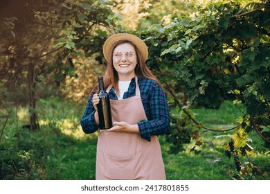 30s Woman in hat tasting red wine in vineyard. Portrait of pretty young woman holding bottle of wine on sunny day. Natural wine industry. Mockup for design - Powered by Shutterstock