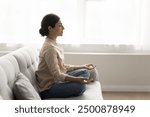 30s woman sit on sofa meditating at home, calming mind, relax body, reducing stress levels, promoting sense of inner peace, improve mental clarity, practicing mindfulness and deep breathing techniques